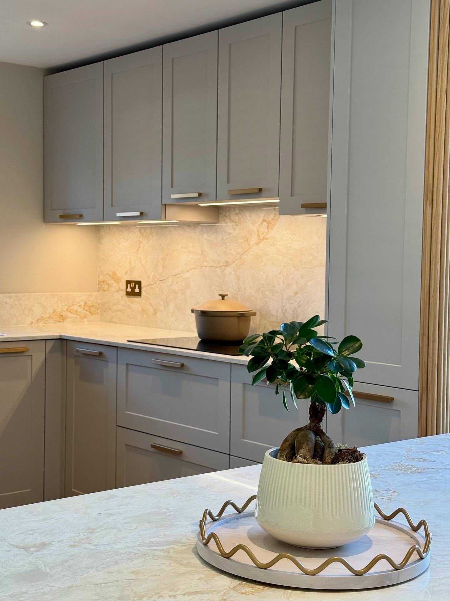 Soft grey Shaker kitchen with brass handles, warm lighting and pale stone-effect worktops