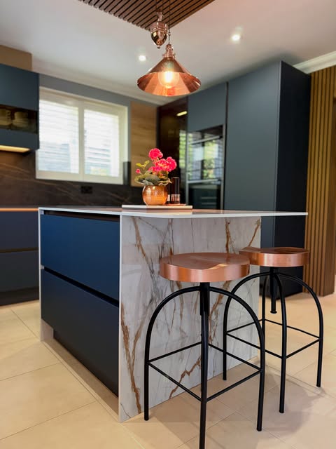 Dark blue cabinetry, a stone-effect island and warm pendant lighting.