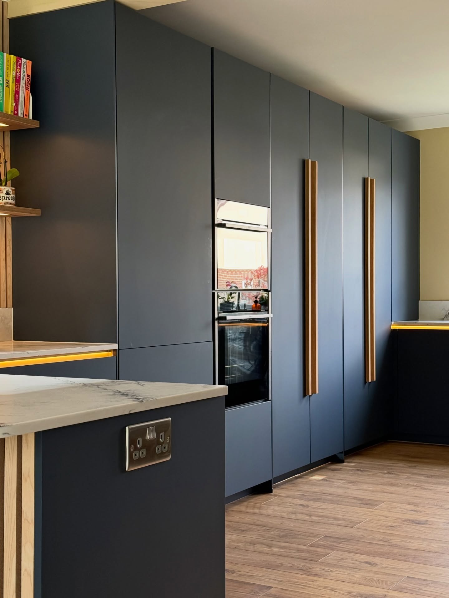 Dark kitchen cabinetry with timber handles, integrated ovens and warm lighting